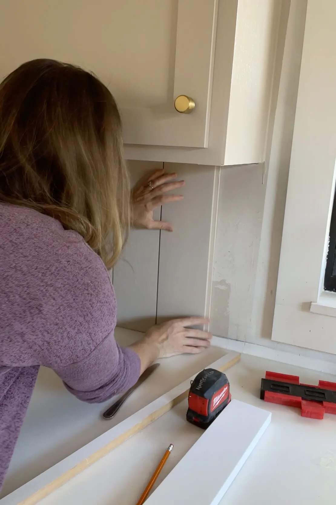 Woman installing a DIY shiplap backsplash.